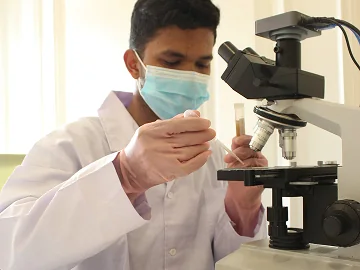 NextBio analyst in lab coat and mask examining a sample tube at a microscope